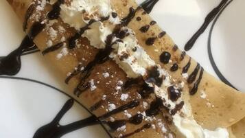 Une crêpe garnie de crème fouettée et nappée de chocolat, présentée sur une assiette.