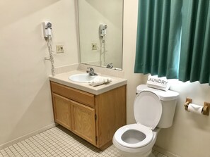 A bathroom with a white sink, wooden vanity, a mirror, a toilet, and a green curtain.