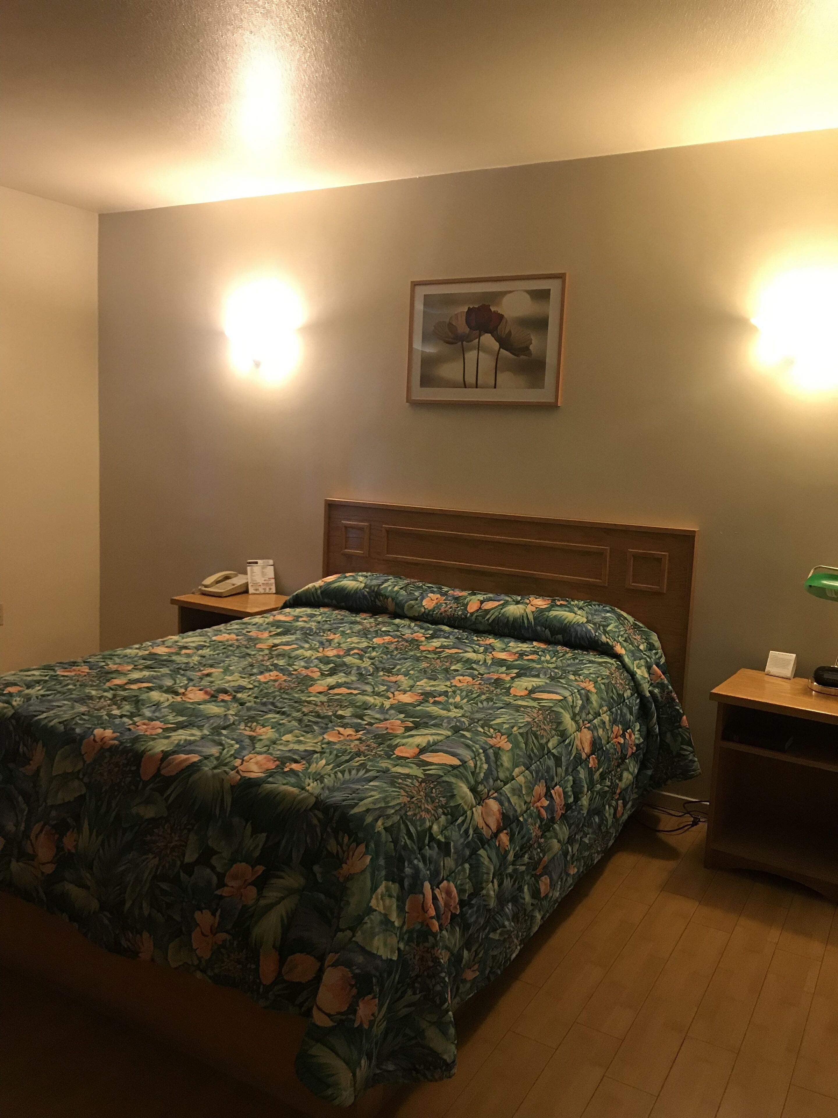 Una camera d'albergo con un letto, un comodino, una lampada e un quadro appeso al muro.