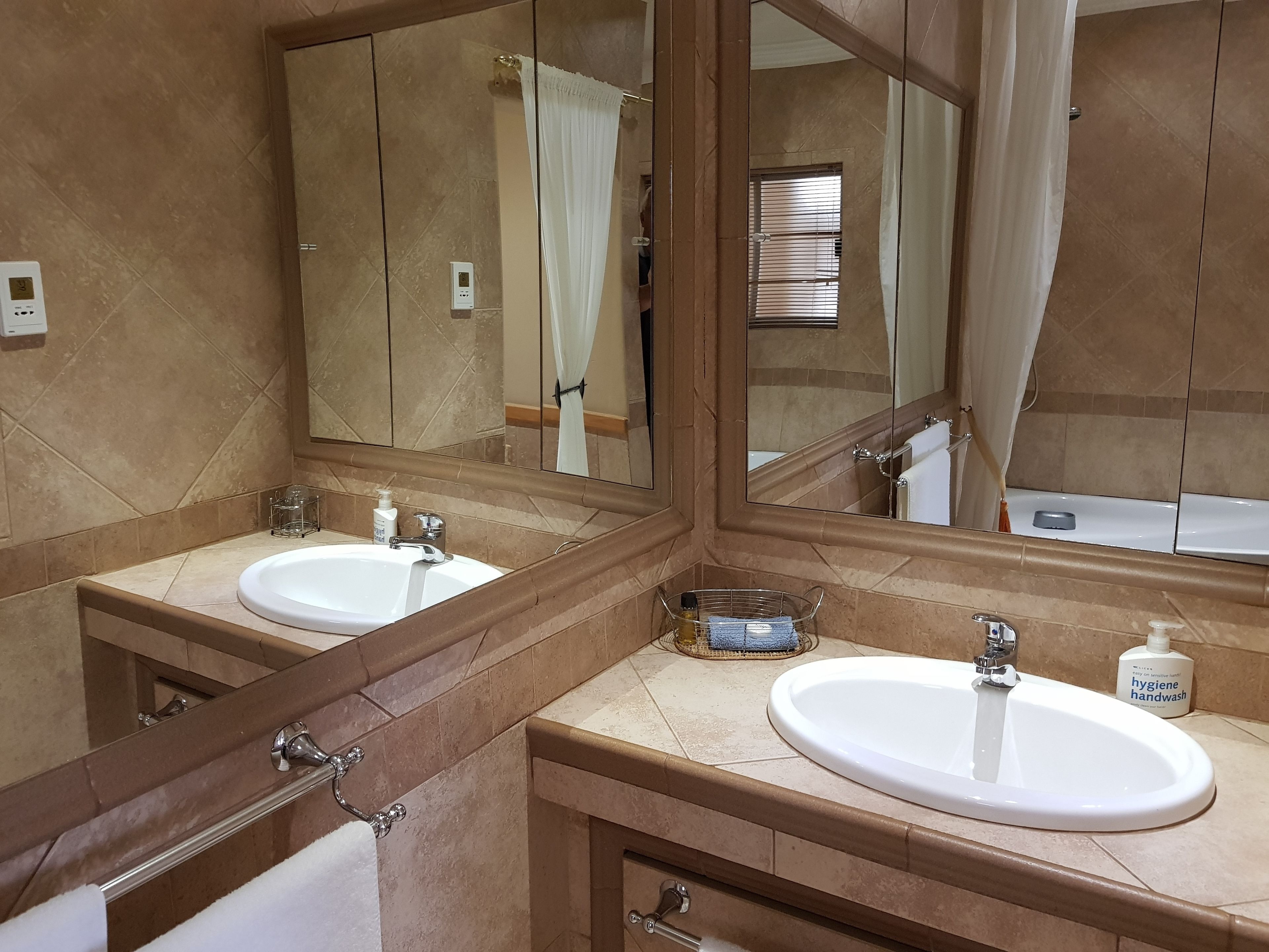 A bathroom with two sinks, a large mirror, and a shower visible in the reflection.