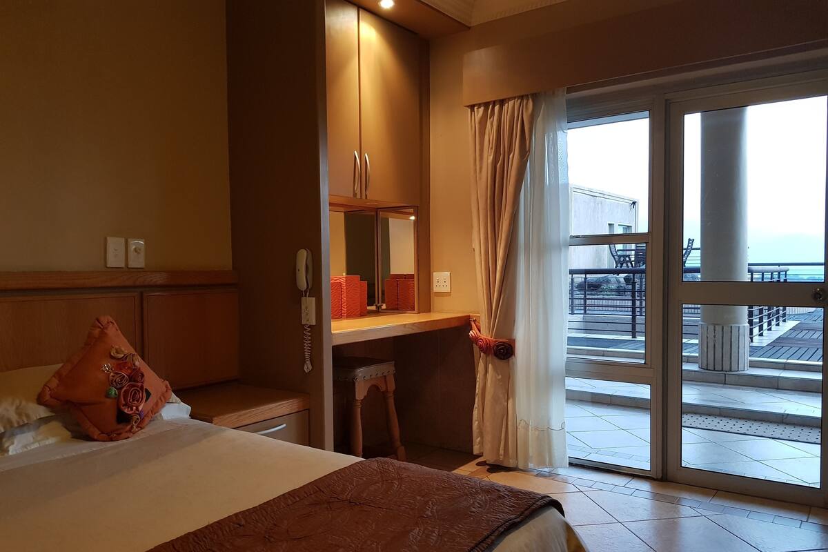 A hotel room with a bed, a desk, a phone, and a view of the outdoor balcony.