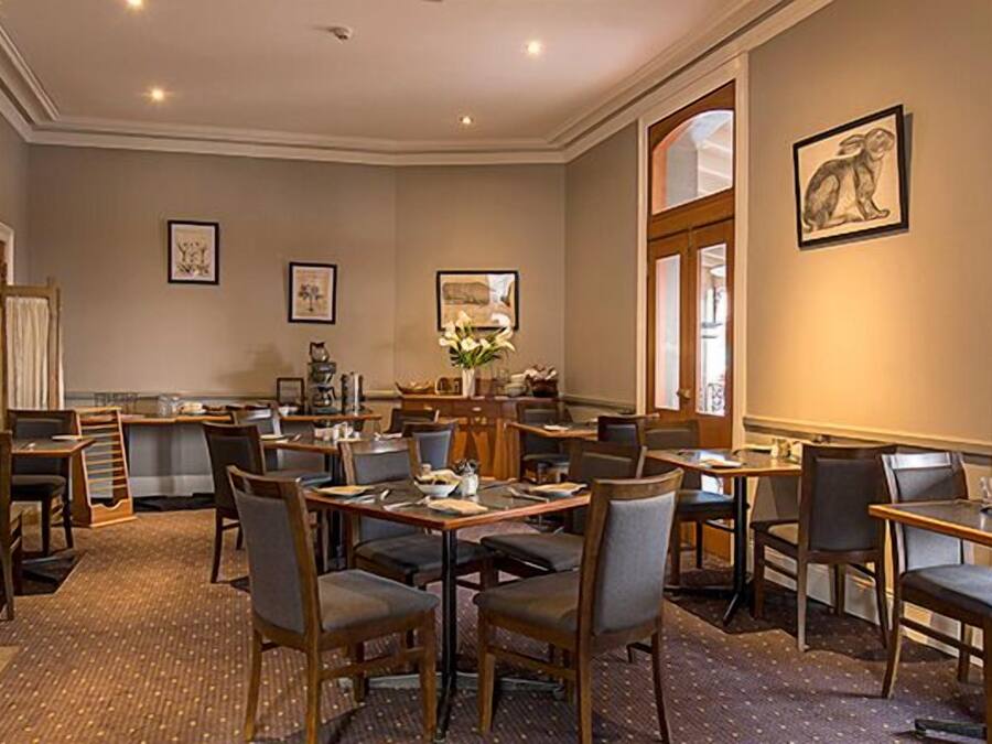A hotel dining area with multiple tables and chairs, a fireplace, and framed artwork on the walls.
