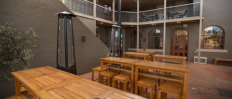 A courtyard with wooden tables and benches, a staircase, and a balcony with railings.