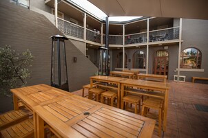 Un patio con mesas y bancos de madera, una escalera y un balcón con barandillas.