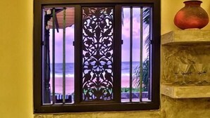 Un baño con un lavamanos, una ventana decorativa con celosía metálica y una estantería con un jarrón y vasos.