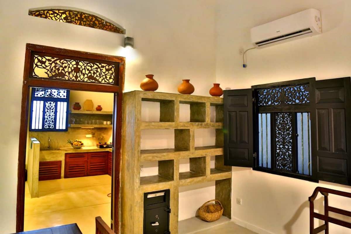 A compact kitchen with a built-in stove, a small dining area, and a decorative shelf with pottery.