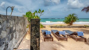 Un área de descanso frente a la playa, con muros de piedra, una piscina y sillones de sol con toallas.