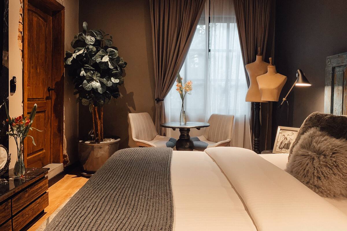 Ein Schlafzimmer mit einem großen Bett, einer Holztür, einem Blumentopf, einem Stuhl, einem Tisch und einer Lampe.