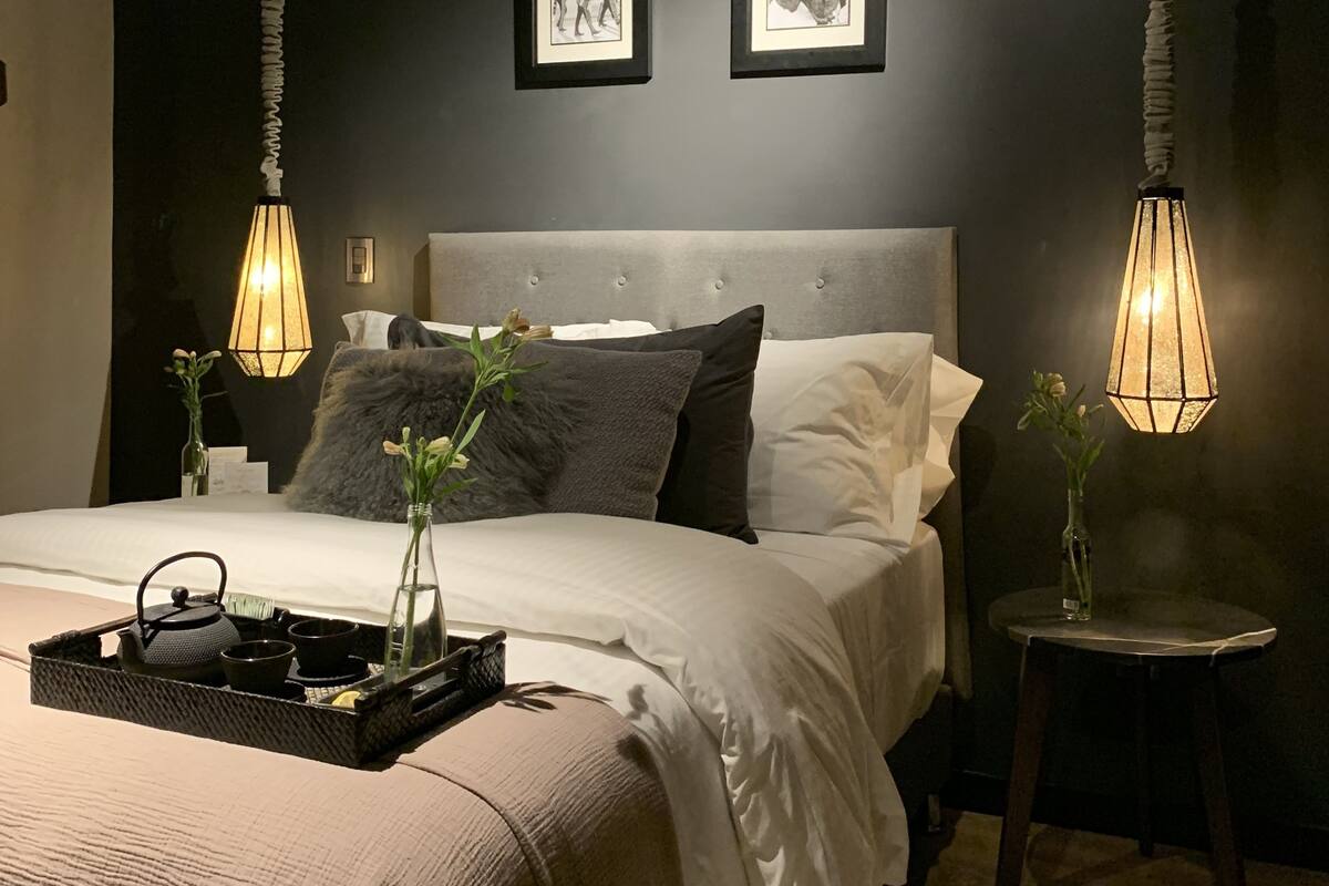 Ein modernes Schlafzimmer mit einem großen Bett, zwei an der Wand befestigten Bilderrahmen, einem Nachttisch mit einer Vase und einer Pendelleuchte.