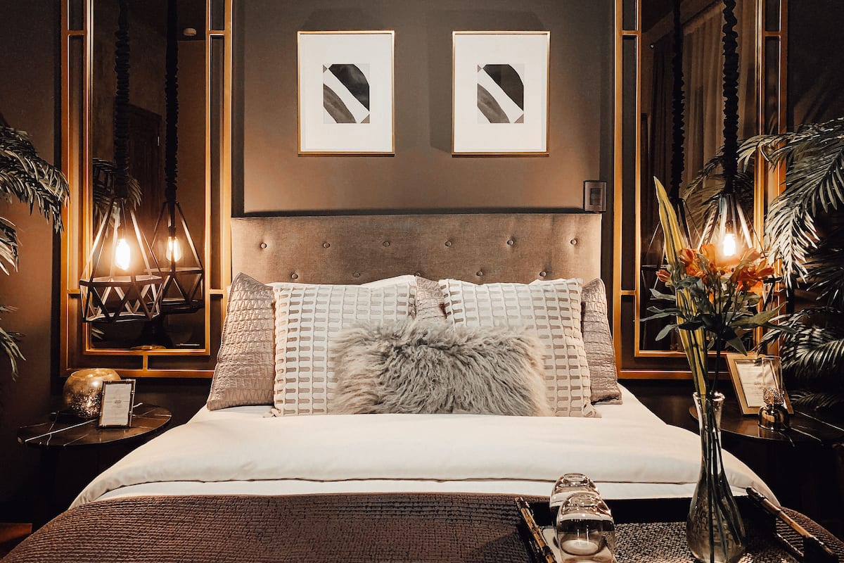 Ein Schlafzimmer mit einem großen Bett, zwei gerahmten Kunstwerken an der Wand, einem Nachttisch mit Lampe und einer Vase mit Blumen.