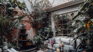 Un jardín interior acogedor con pared de ladrillo, una fuente y una zona de estar con cojines y velas.