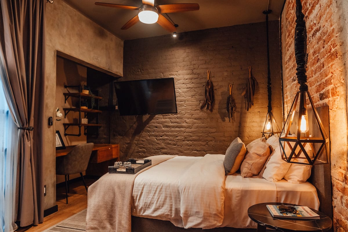 Ein gemütliches Schlafzimmer mit Bett, Schreibtisch, Fernseher und einer Ziegelwand.