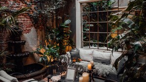 Un espacio interior acogedor con pared de ladrillo, ventana con diseño de cuadrícula y zona de estar con mesa de centro y cojines.
