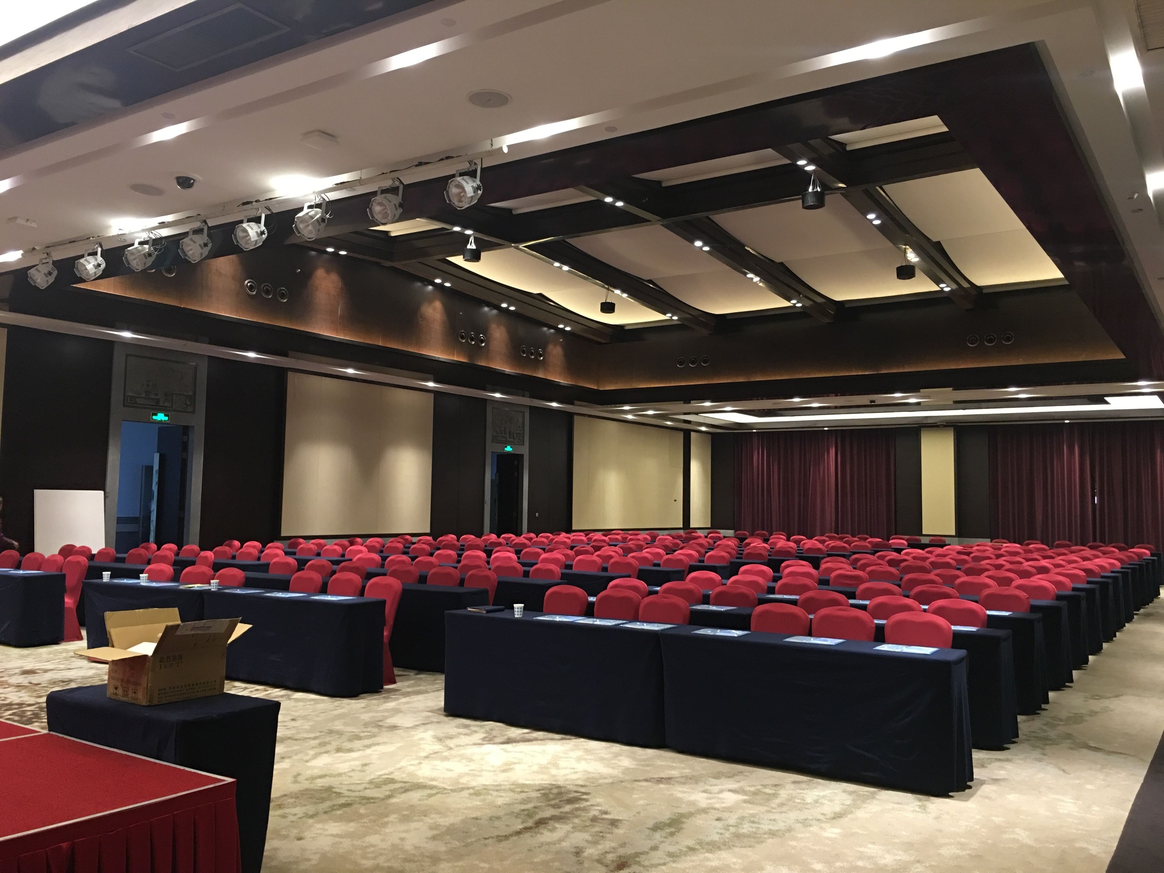 A conference room with rows of red chairs, black tables, and a carpeted floor.