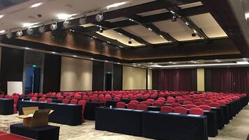 A conference room with rows of red chairs, black tables, and a carpeted floor.