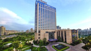 A high-rise building with a modern architectural design, surrounded by landscaped gardens and a parking area.