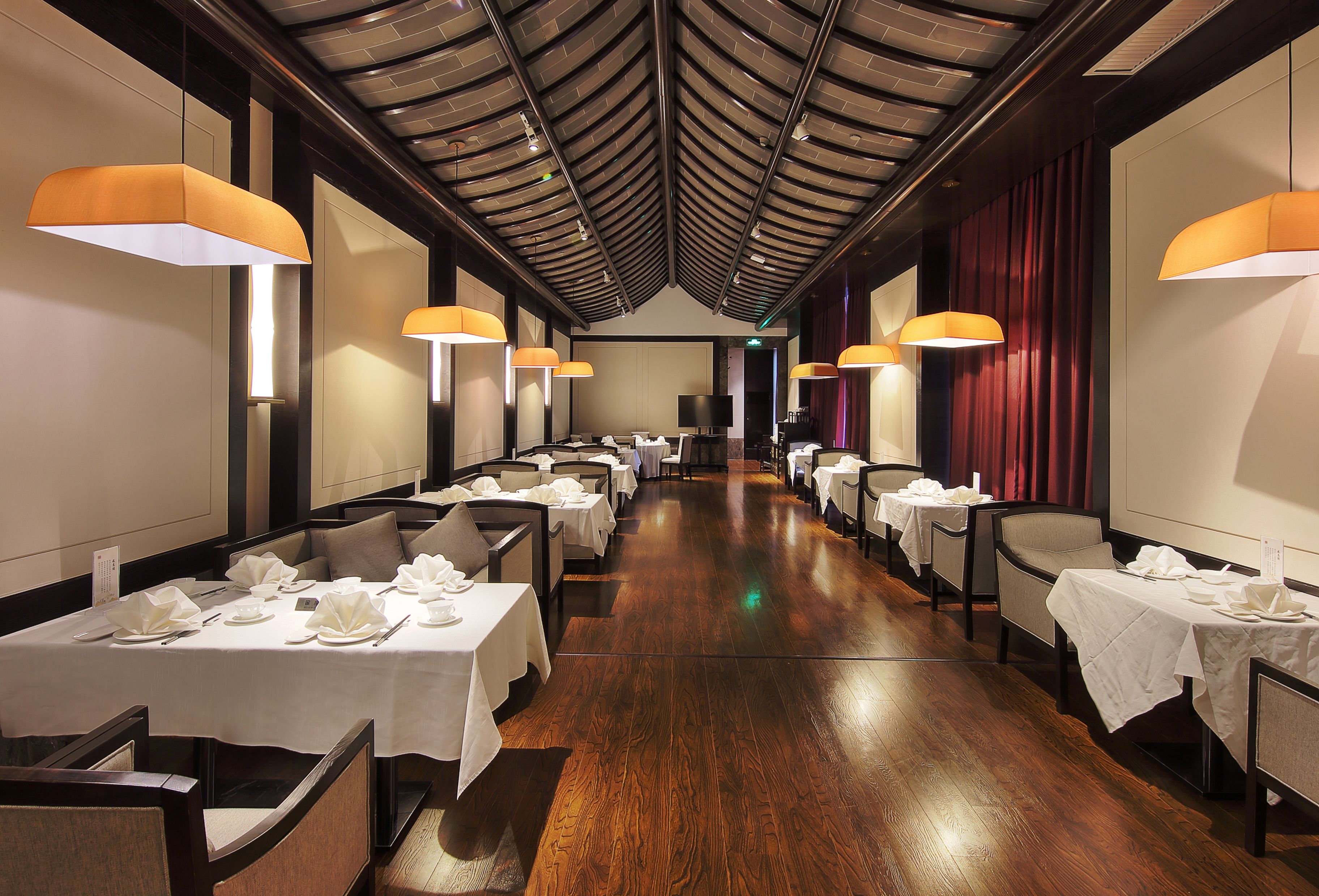 A restaurant with tables set for dining, featuring a wooden floor and a high ceiling with exposed beams.