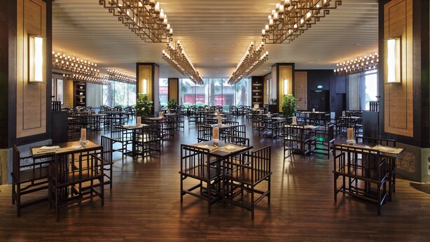 A spacious dining area with multiple tables and chairs, a modern ceiling design, and large windows allowing natural light.
