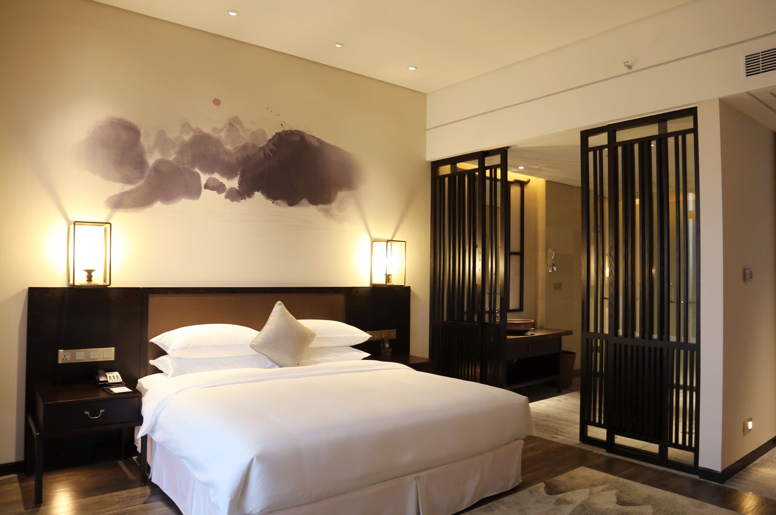 Ein Hotelzimmer mit einem großen Bett, Nachttischlampen, einem Wandbild und einer traditionellen Schiebetür.