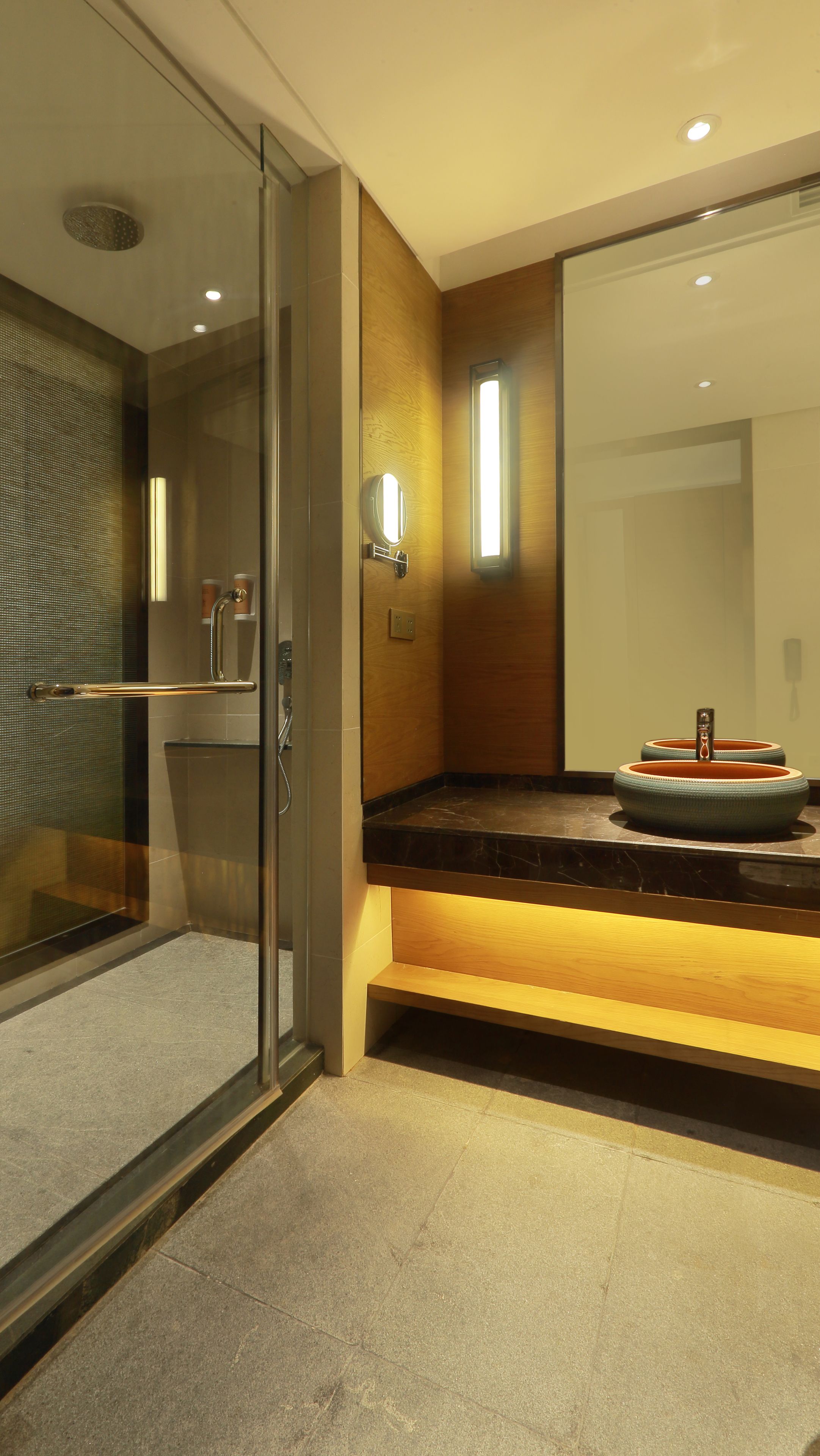 A modern bathroom with a glass-enclosed shower, a wooden vanity with a round sink, and a large mirror.