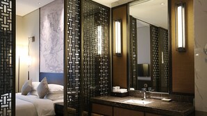 A modern hotel room with a bed, a bathroom with a sink and mirror, and decorative panels.