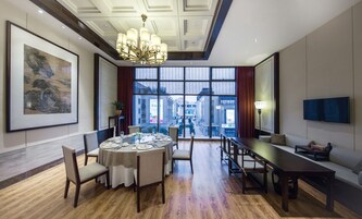 Un comedor con una mesa redonda dispuesta para cuatro personas, rodeada de sillas, una larga mesa con bancos y una lámpara de araña.