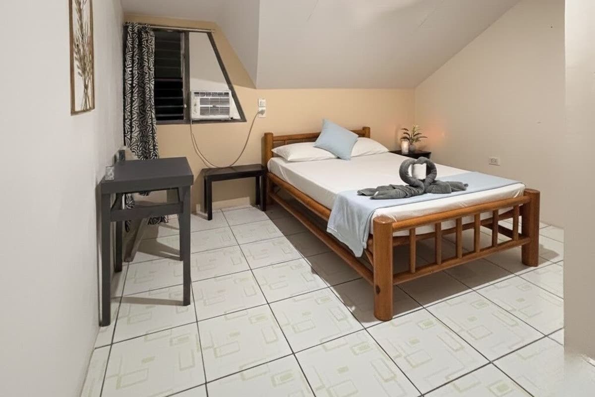 A small, well-lit bedroom with a bed, bedside table, and a desk.