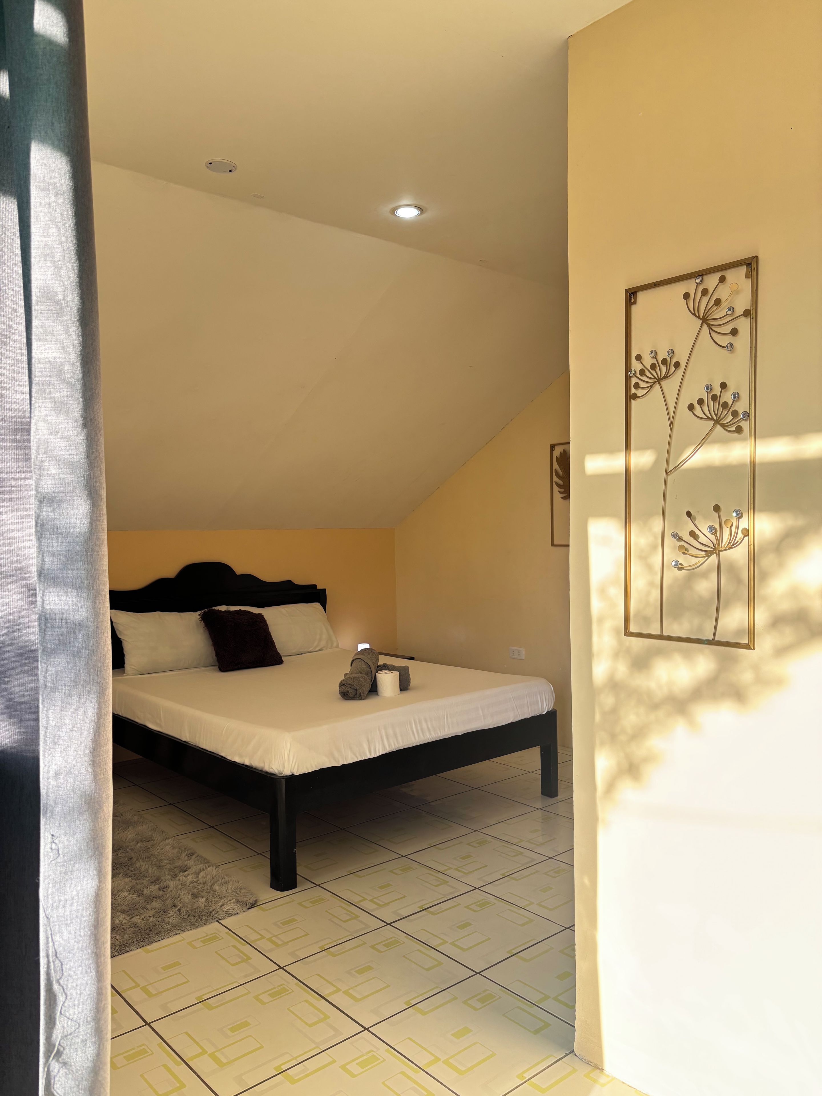 A bedroom with a bed, a ceiling light, a wall-mounted artwork, and a window with curtains.