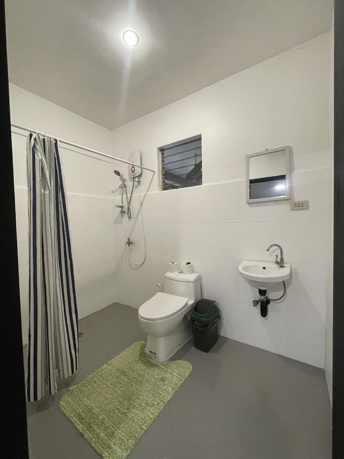 A bathroom with a toilet, sink, shower, and a small window.