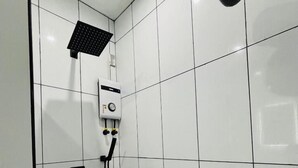 A bathroom with white tiled walls, a showerhead, a control panel, and a black pipe. - Hotel Sisters Inn  Moalboal (Moalboal)