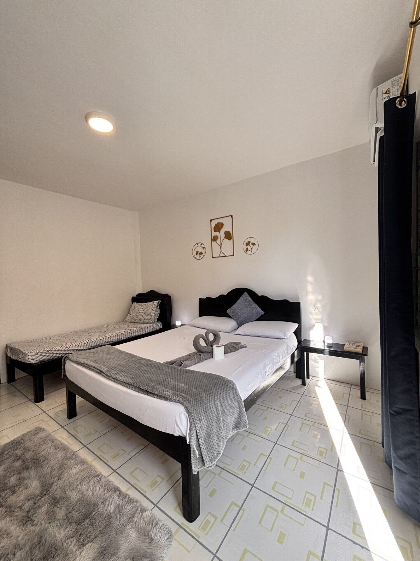 Ein Schlafzimmer mit zwei Betten, einem Nachttisch, einer Wandleuchte und einem Fenster mit Vorhängen.