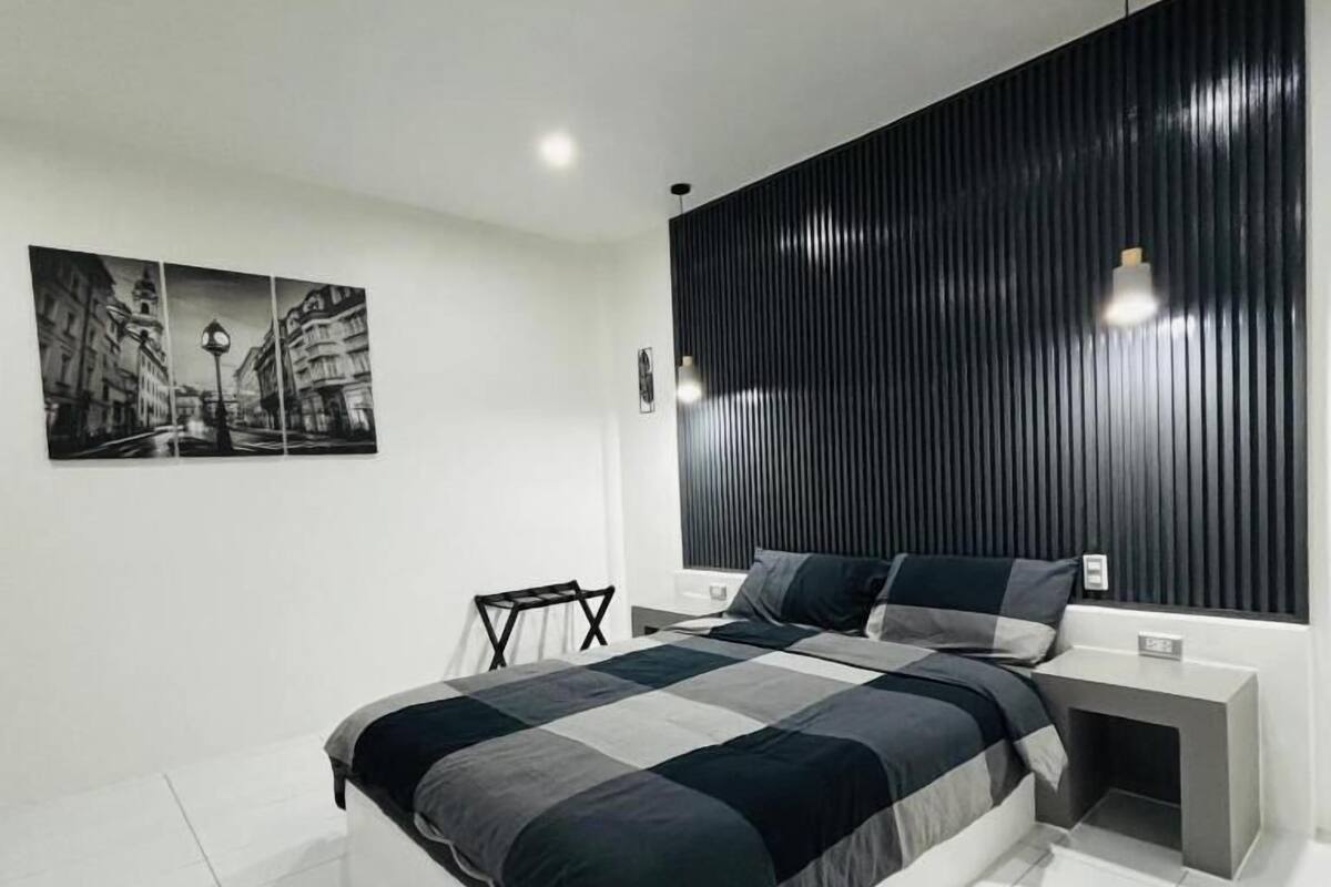 A modern bedroom with a large bed, a black headboard, and a cityscape artwork on the wall.