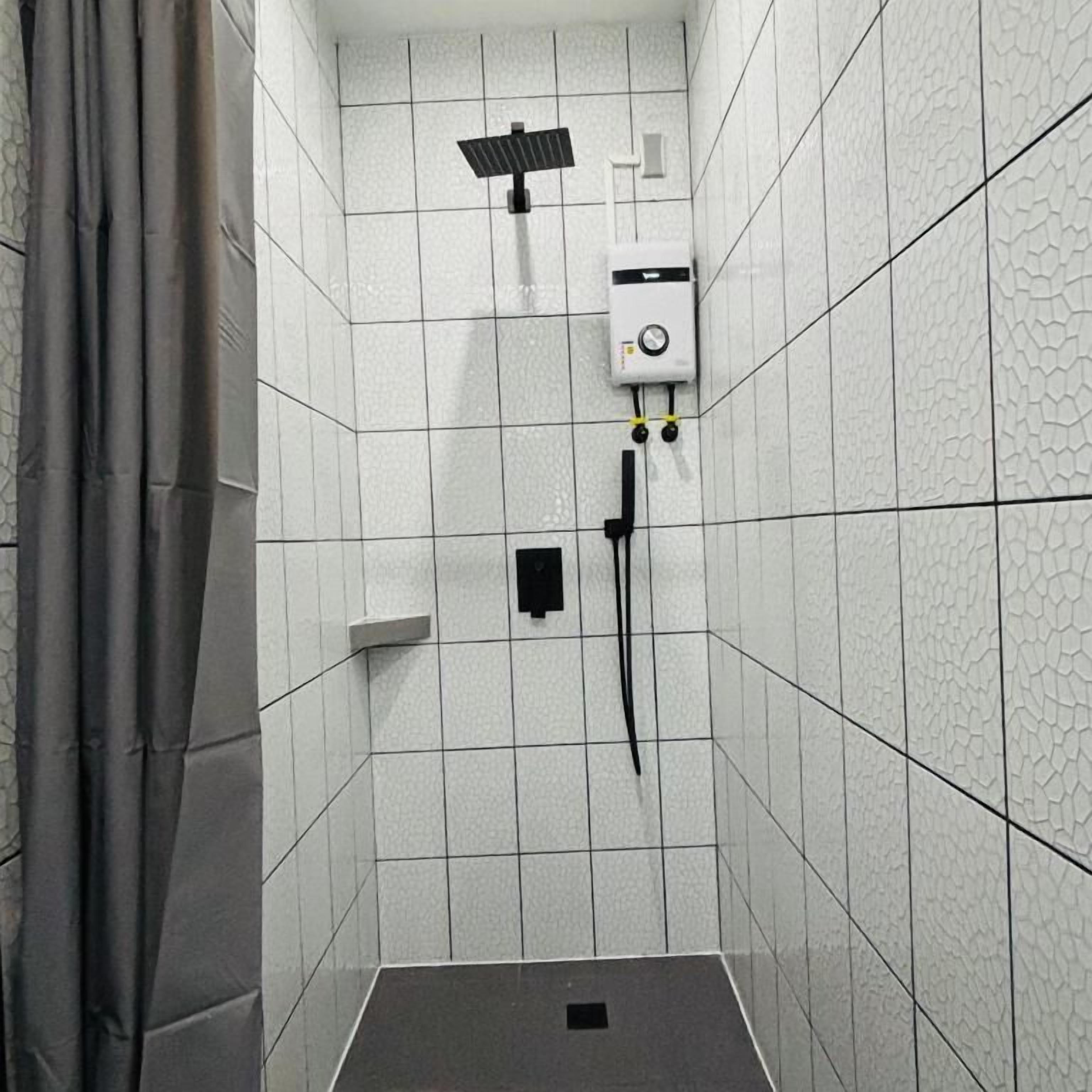 Un baño pequeño con azulejos, un cabezal de ducha, un panel de control y un desagüe.