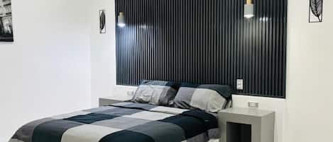 A modern bedroom with a large bed, a dark headboard, bedside tables, and a white tiled floor.