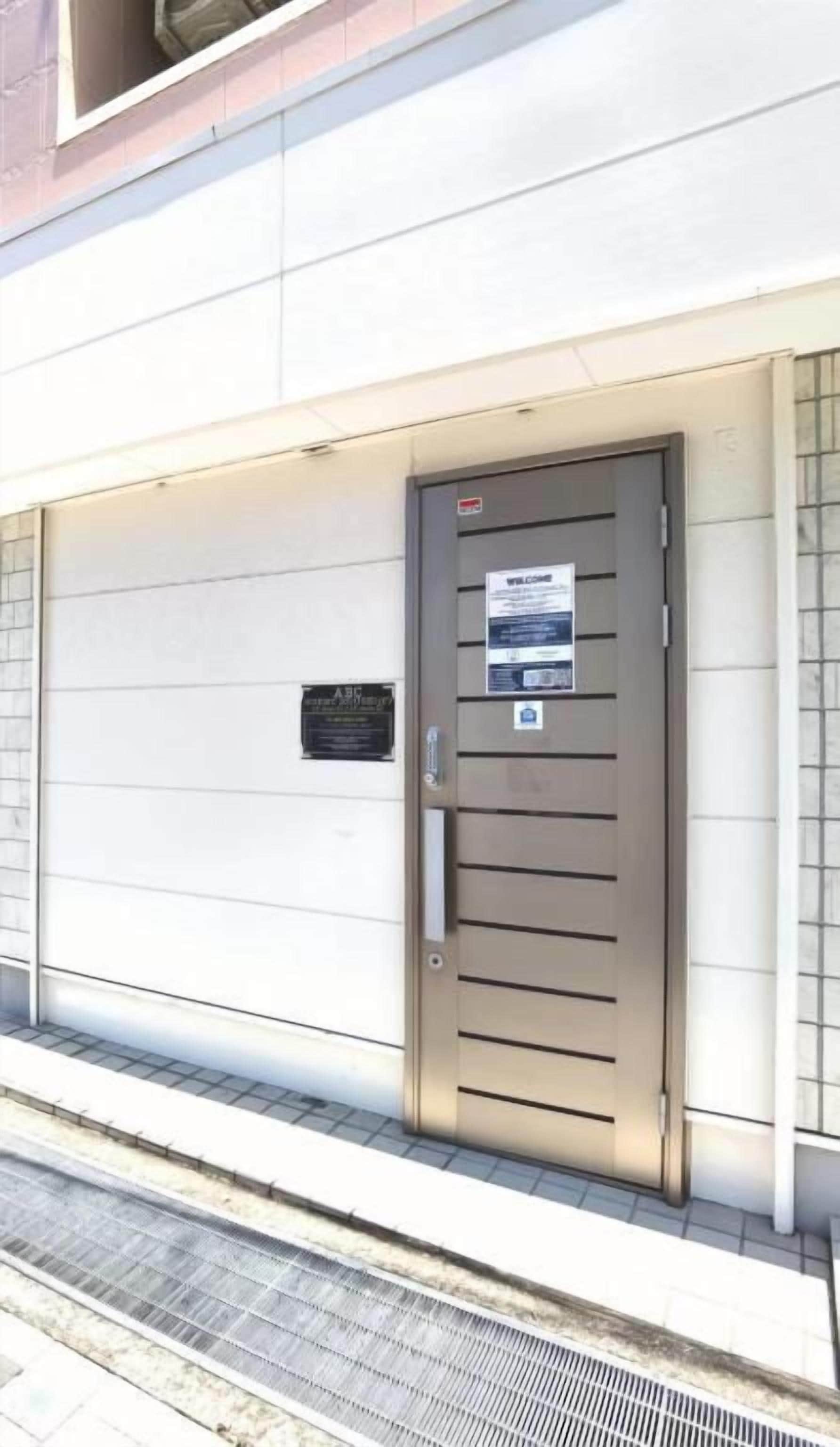 Puerta metálica cerrada con un letrero, una placa pequeña y una rejilla metálica en el suelo.