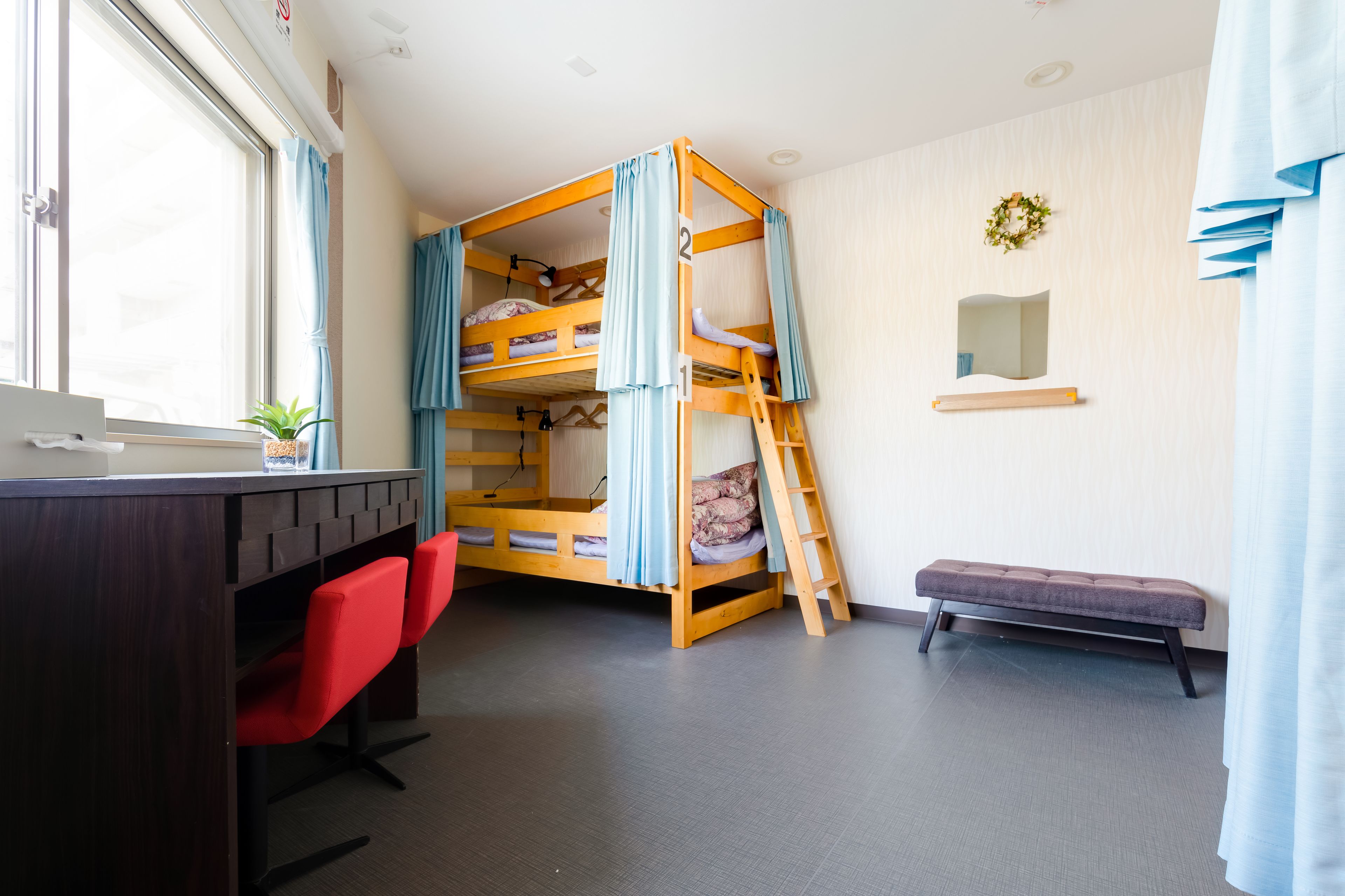 Un lit superposé avec un bureau et des chaises, un banc et un petit miroir accroché au mur.