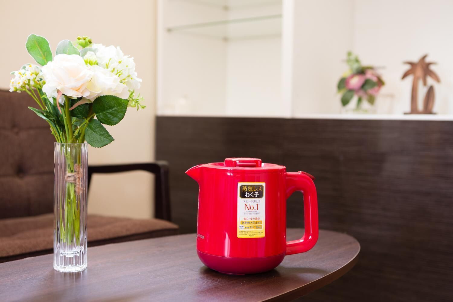 Una tetera roja sobre una mesa, con un florero transparente a la izquierda.