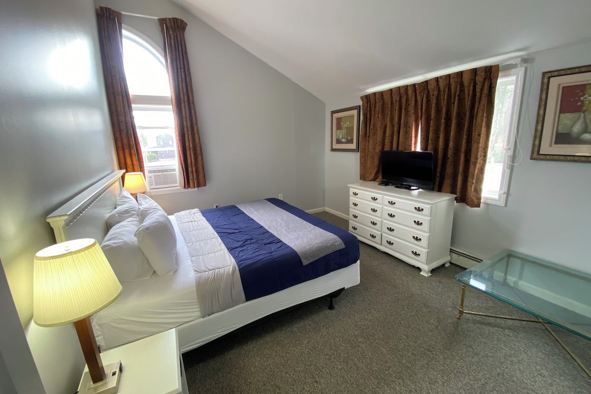 A bedroom with a bed, a dresser, a television, and a glass table.