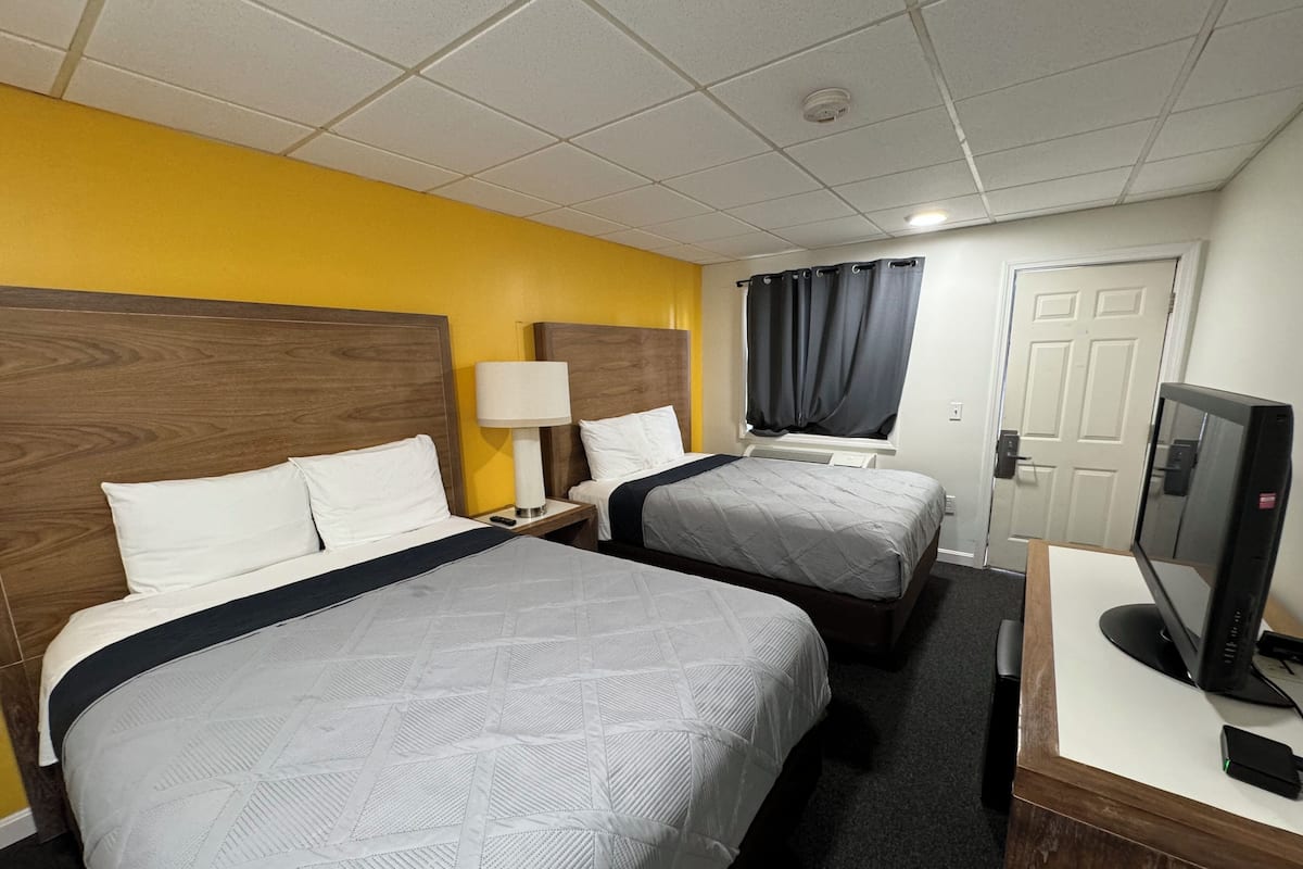 A hotel room with two beds, a desk with a computer, a lamp, and a TV.