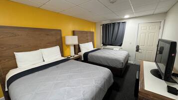 A hotel room with two beds, a desk with a computer, a lamp, and a TV.