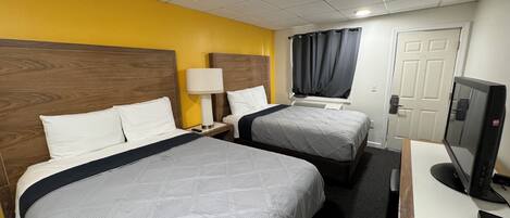 A hotel room with two beds, a desk with a computer, a lamp, and a TV.