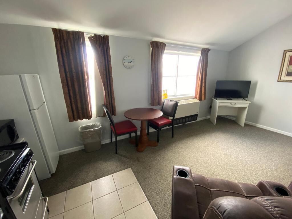 A compact living space with a kitchenette, a dining area with a table and chairs, a television, and a window with curtains.