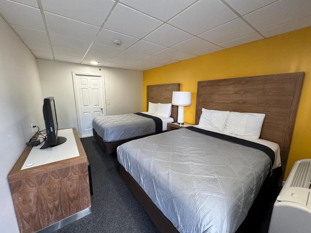 Et hotelværelse med to senge, et skrivebord med en computer, en lampe og en varmeovn.
