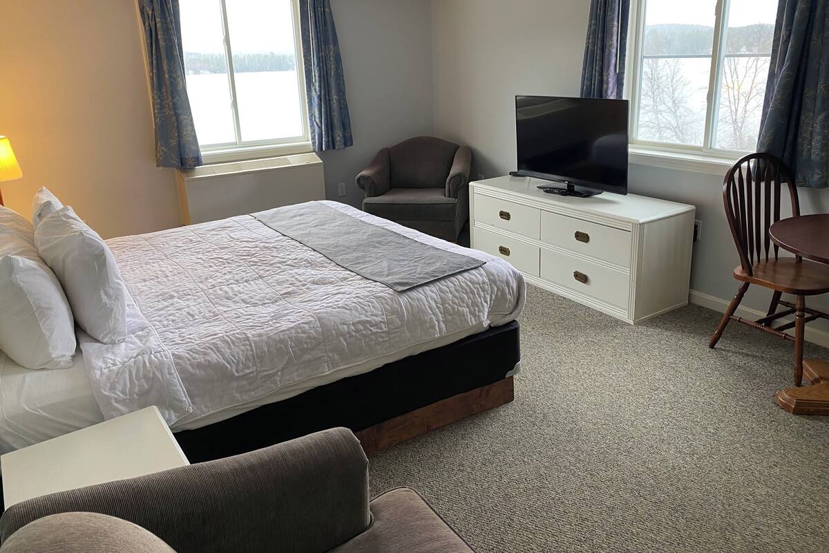 A hotel room with a bed, a TV on a dresser, a chair, and a view of the outdoors.