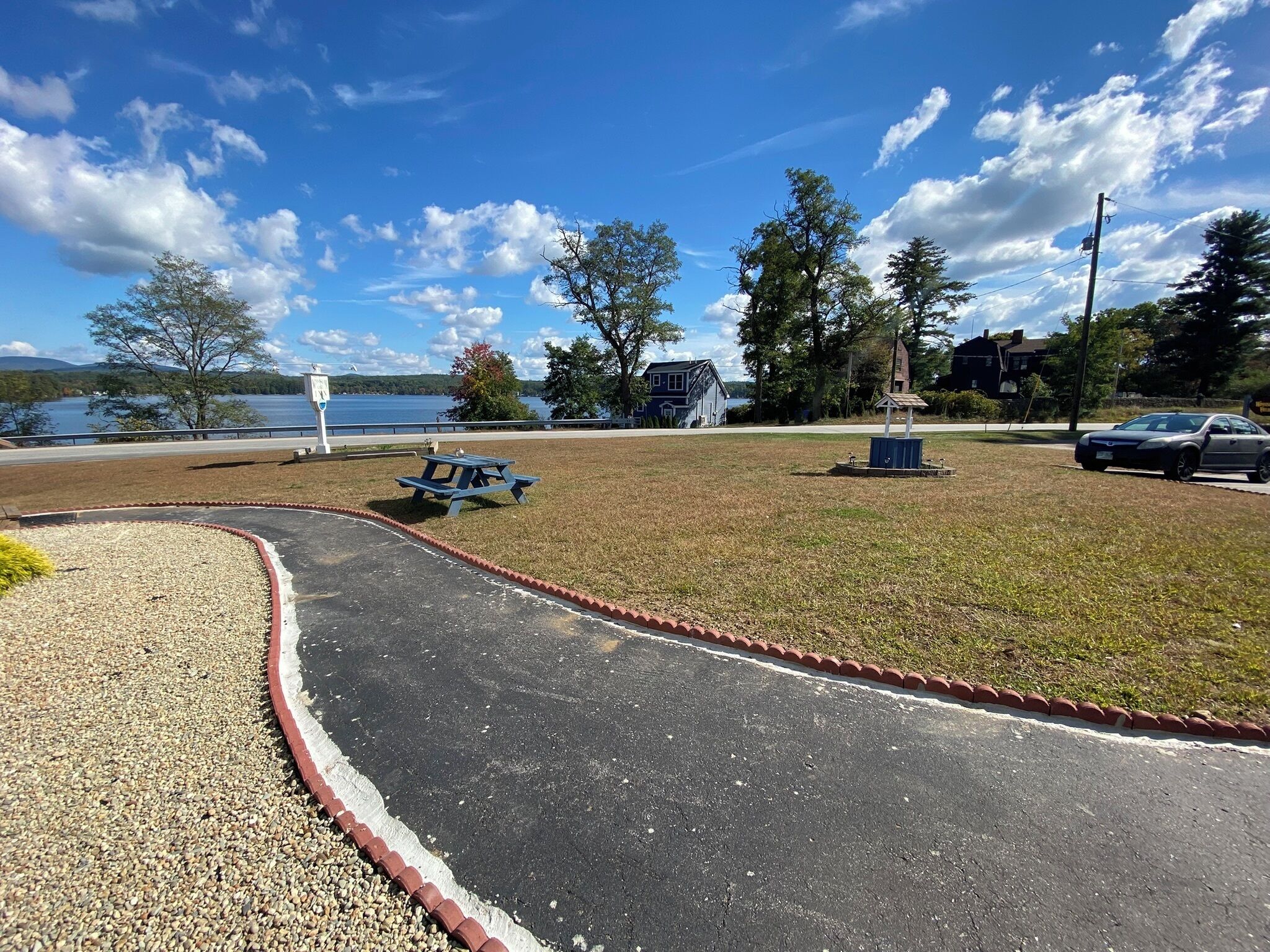 A picnic area with a bench and a small fountain, surrounded by grass and a gravel path.