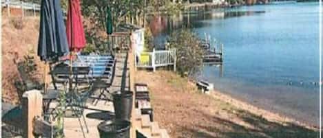 A lakeside patio with outdoor furniture and umbrellas, a dock, and a view of the lake.