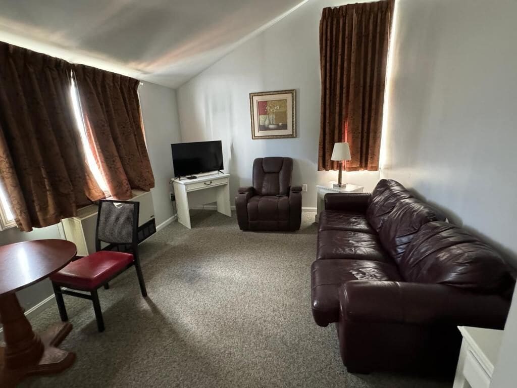 Una sala de estar con un sofá de cuero marrón, un televisor sobre un mueble bajo, un escritorio y una silla.