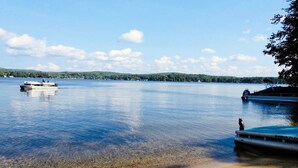 A calm lake with clear water, a boat docked on the right, and a stone bench on the sandy shore. - Winnisquam Lake Inn (Tilton)