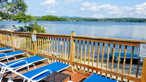 A deck with blue lounge chairs and a wooden railing overlooking a lake. - Winnisquam Lake Inn (Tilton)