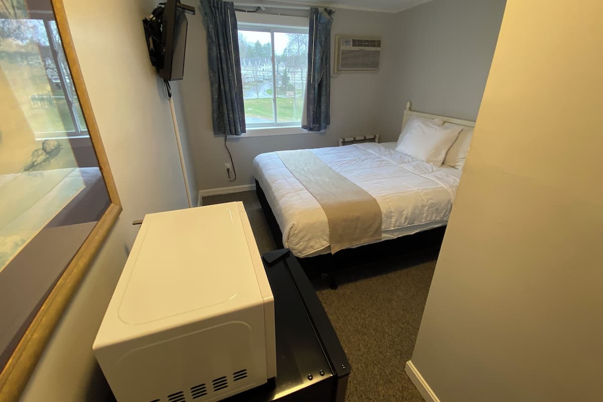 A bedroom with a bed, a TV mounted on the wall, and a window with curtains.